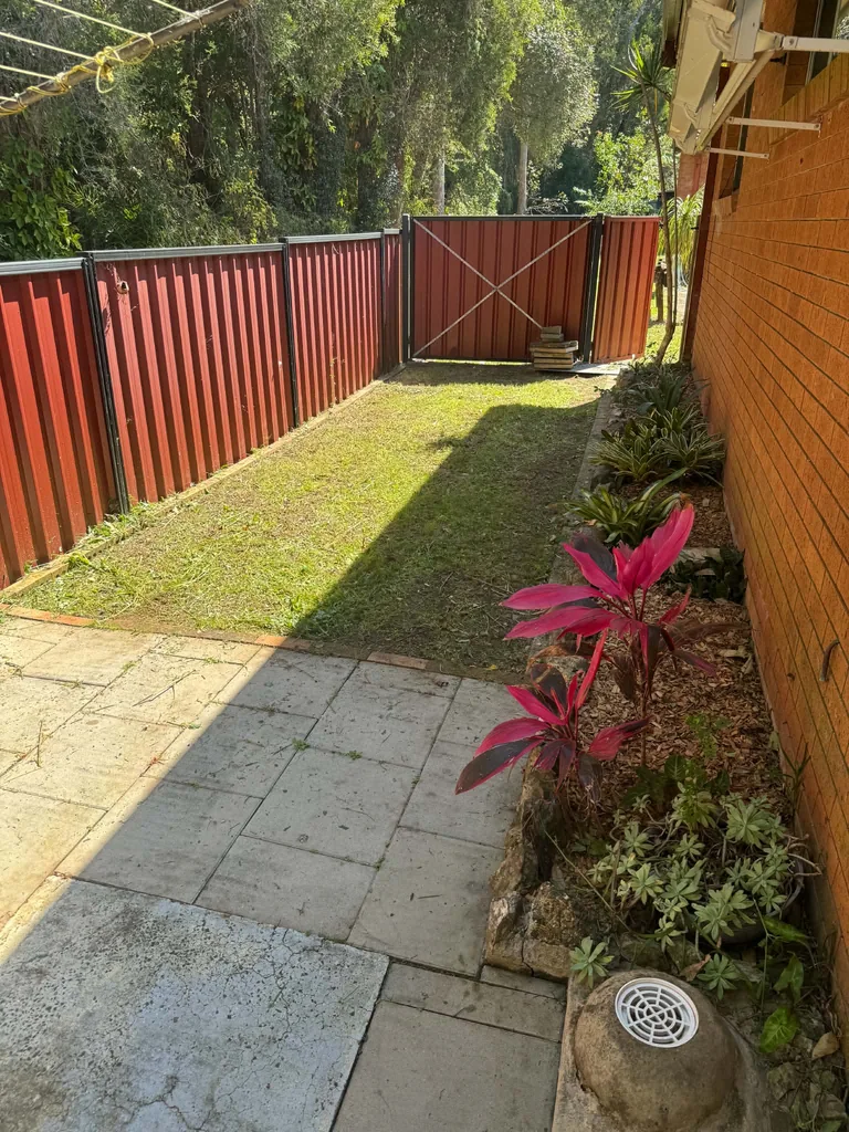 Side lawn and garden bed between a brick house and metal fence
